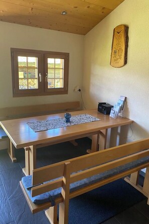 A wooden dining table with benches, a clock on the wall, and a window with a view of the outdoors. - Alphütte Bielerhüs Appartement/Fewo, Dusche, WC 3 Zimmerwohnung, 4-Betten by Interhome (Fiesch)