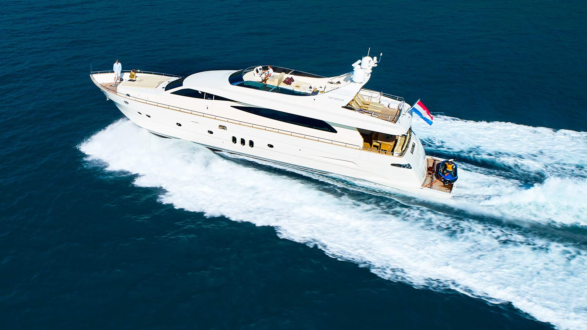 A large yacht with multiple decks, a flag, and a wake behind it.