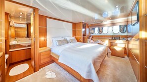 A modern, compact bedroom with a large bed, wooden cabinetry, a vanity with a mirror, and a small seating area.