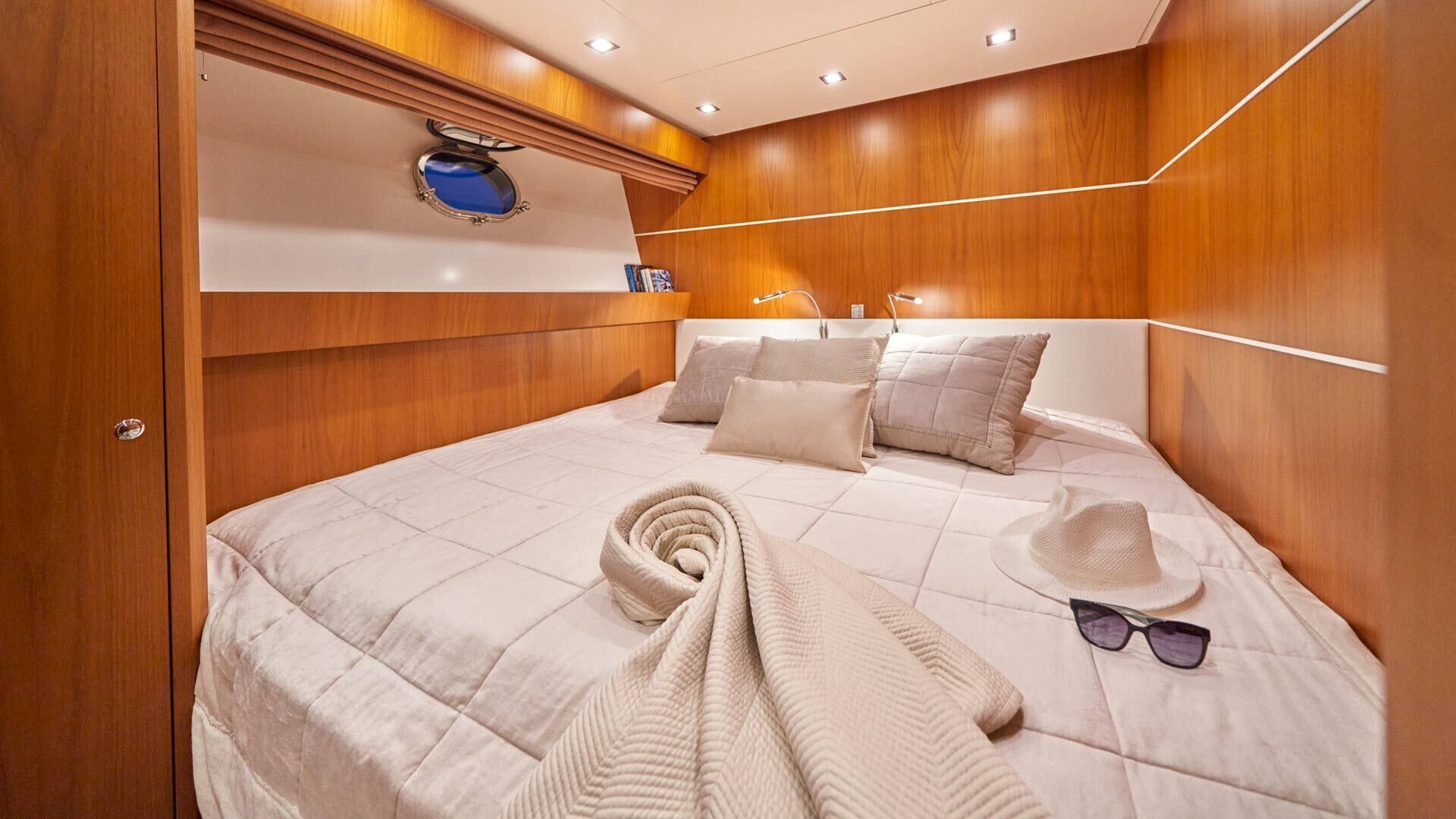 Ein Schlafzimmer mit einem hölzernen Kopfende, einem ordentlich bezogenen Bett mit Kissen, einem zusammengerollten Handtuch, einem Hut und einer Sonnenbrille auf dem Bett.