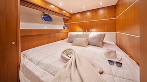Un dormitorio con cabecera de madera, cama con sábanas bien tendidas y almohadas, una toalla enrollada, un sombrero y gafas de sol sobre la cama.