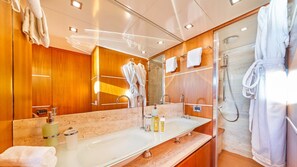 A modern bathroom with a large mirror, wooden paneling, a glass shower enclosure, and a vanity with a sink and toiletries.
