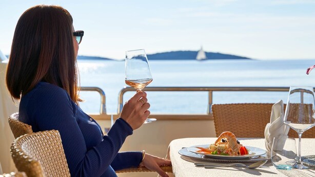 Eine Person isst an einem Tisch mit Blick auf das Meer und ein Segelboot in der Ferne.
