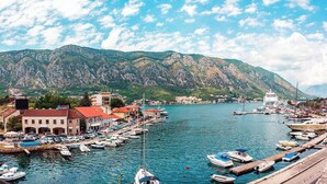 Un port de plaisance avec des bateaux amarrés, une ville avec des bâtiments et des montagnes en arrière-plan.