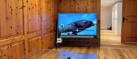 A room with wooden paneling, a television on a stand, and a glass coffee table with a Monopoly game box and magazines.