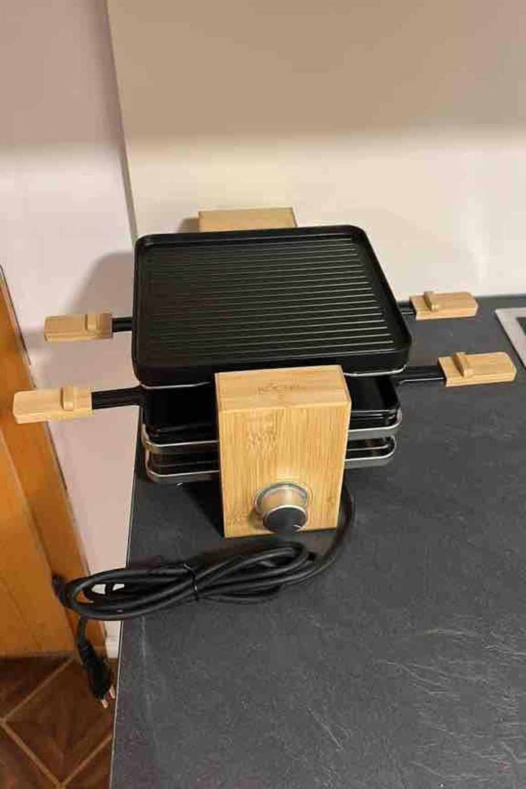 A portable grill with a wooden handle and a black cooking surface, placed on a dark countertop.