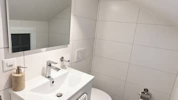 Et moderne badeværelse med en hvid kommode, et stort spejl, et hvidt toilet og et bruseområde.