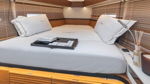 A compact, modern bedroom with a skylight, wooden paneling, a neatly made bed, and a bedside table with a lamp and candles. - Sun-Kissed Sailing Adventure in Islas Sarónicas (Piraeus)