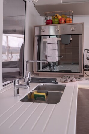 Eine moderne Küche mit Spüle aus Edelstahl, integriertem Backofen und Obstkorb auf der Arbeitsfläche.