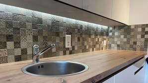 Ett kök med en modern diskho i rostfritt stål, en bänkskiva i trä och ett dekorativt mosaikmönster på väggen bakom diskhon.
