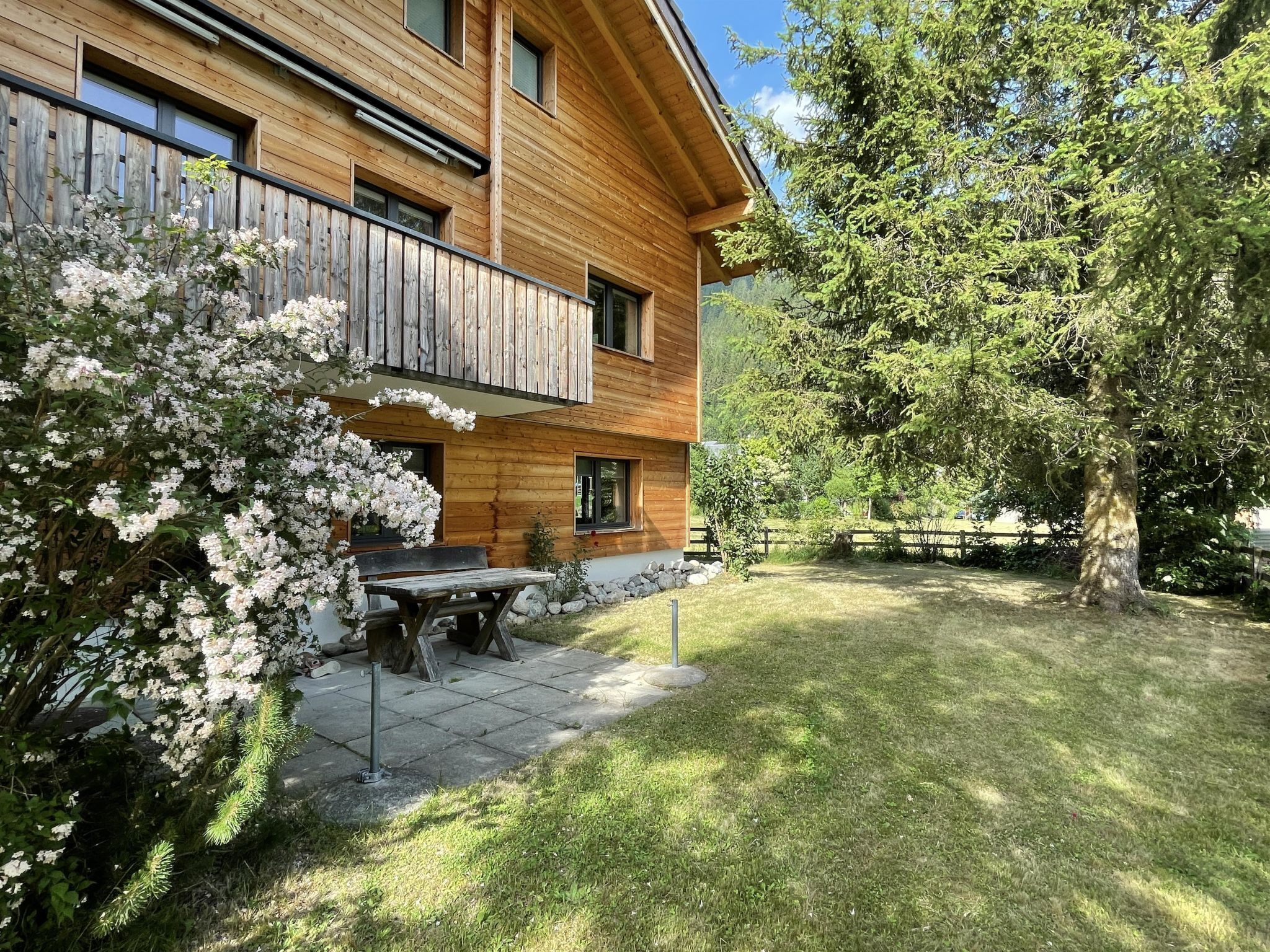 Ein Holzhaus mit Balkon, einer Terrasse, einem Tisch und Stühlen sowie einem gepflegten Rasen.