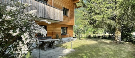 Une maison en bois avec un balcon, une terrasse avec une table et des chaises, et une pelouse bien entretenue.