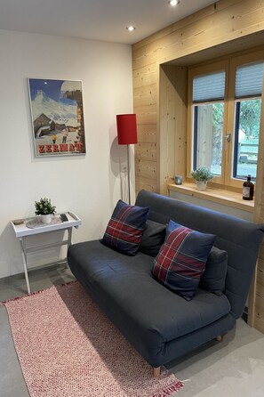 A modern living room with a dark grey sofa, two plaid cushions, a red floor lamp, a small table with a plant, and a poster on the wall. - Ilse EG Süd-West Appartement/Fewo, Dusche oder Bad, WC 3 Zimmerwohnung, 3-Betten by Interhome (Fiesch)