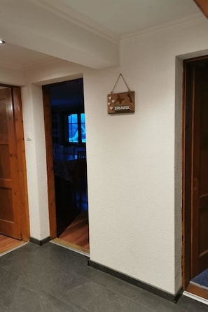 A hallway with a wooden door on the left, a wooden wall with a 'ZUHAUSE' sign, and a dark room in the background.