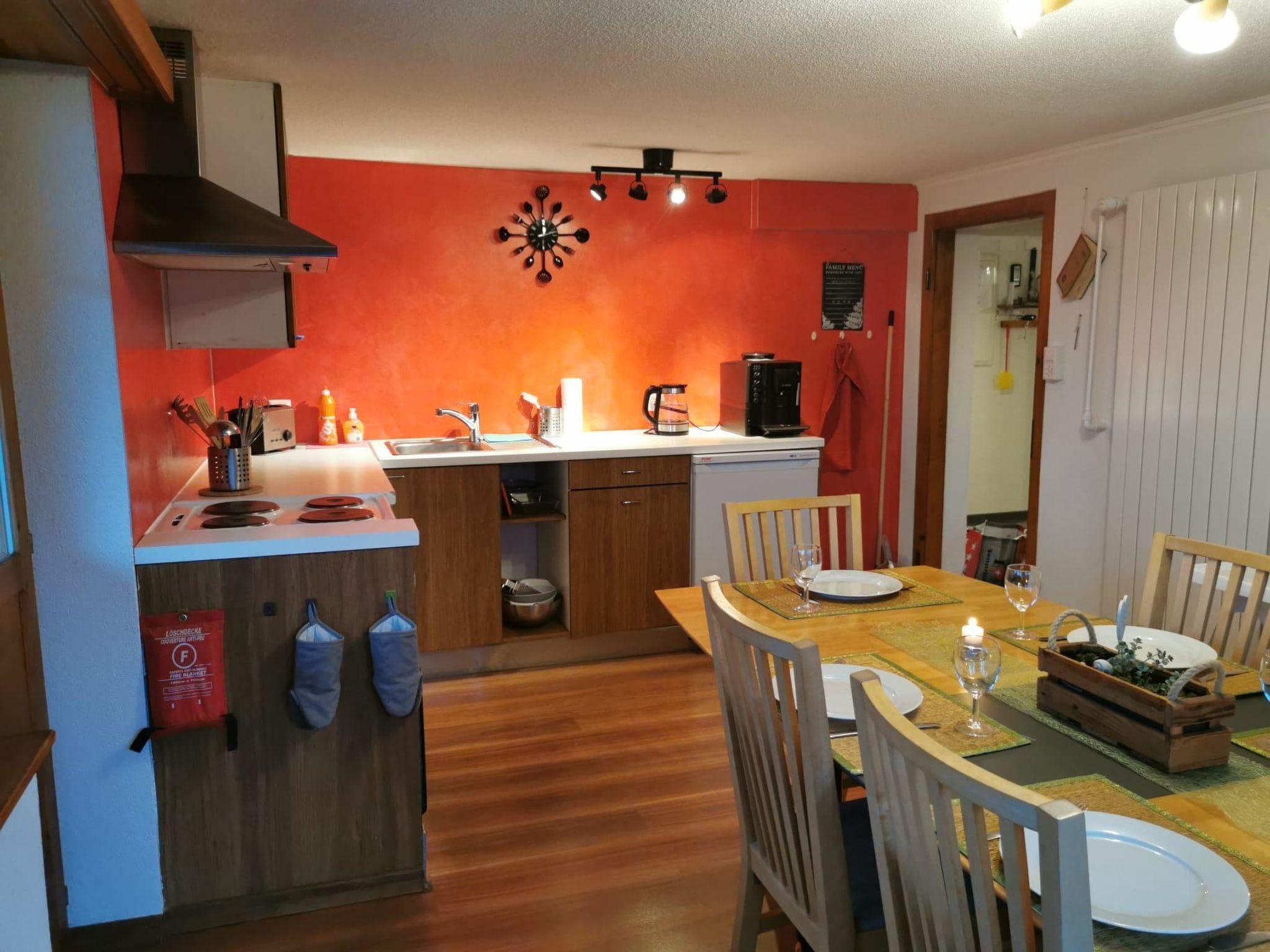 Una cocina compacta con una isla central, un comedor con sillas de madera y una pared de acento roja.