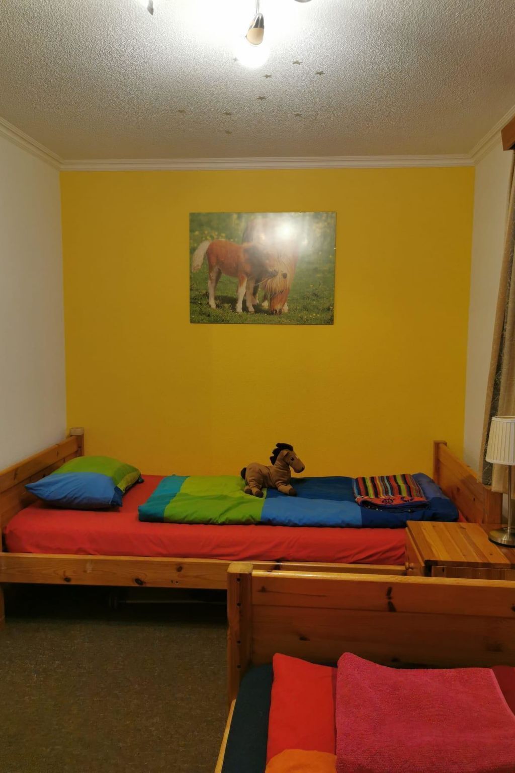 Een kleine kamer met een enkel bed, een houten hoofdbord, een nachtkastje en een lamp.