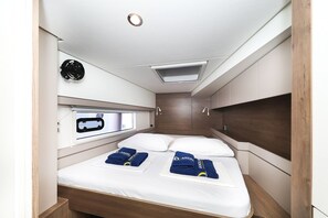 Een compacte, goed verlichte kamer met een bed, twee kussens, een hoofdbord, een raam met uitzicht en een apparaat aan de muur.