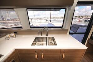 Een moderne keuken met een roestvrijstalen spoelbak, houten keukenkastjes en een raam met uitzicht op een jachthaven.