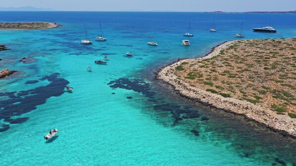 A coastal area with boats, clear turquoise water, rocky terrain, and a small island.