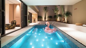 Una piscina interior con un flotador de flamenco rosa, rodeada de plantas y un diseño de interiores moderno.