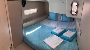 Cabine compacta e bem iluminada, com beliche, uma pequena janela e toalhas organizadamente dispostas.