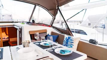 A boat's dining area with a table set for two, a sink, and a view of the marina.