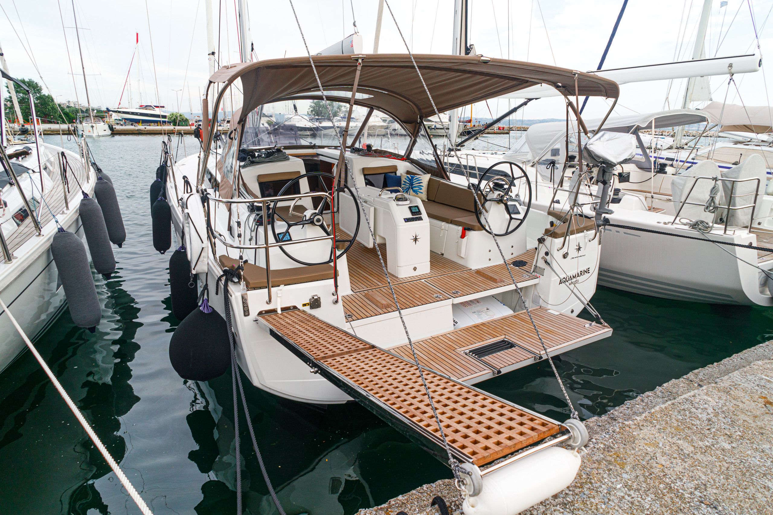 Un velero amarrado en un puerto deportivo, con cubierta techada, timón y una pequeña zona de camarote.