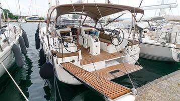 Un velero amarrado en un puerto deportivo, con cubierta techada, timón y una pequeña zona de camarote.