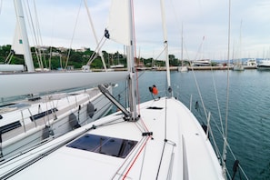A marina with multiple sailboats docked, featuring a clear view of the water and a distant shoreline with buildings.