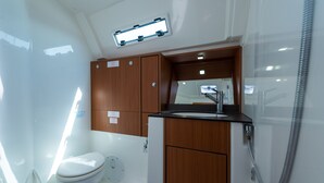 A compact bathroom with a white toilet, wooden cabinets, a sink with a mirror, and a shower. - Macedonian Sun and Beach Sailing Extravaganza from Kavala (Kavala)
