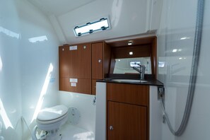 Une petite salle de bain avec des toilettes blanches, des meubles en bois, un lavabo avec un miroir et une douche.
