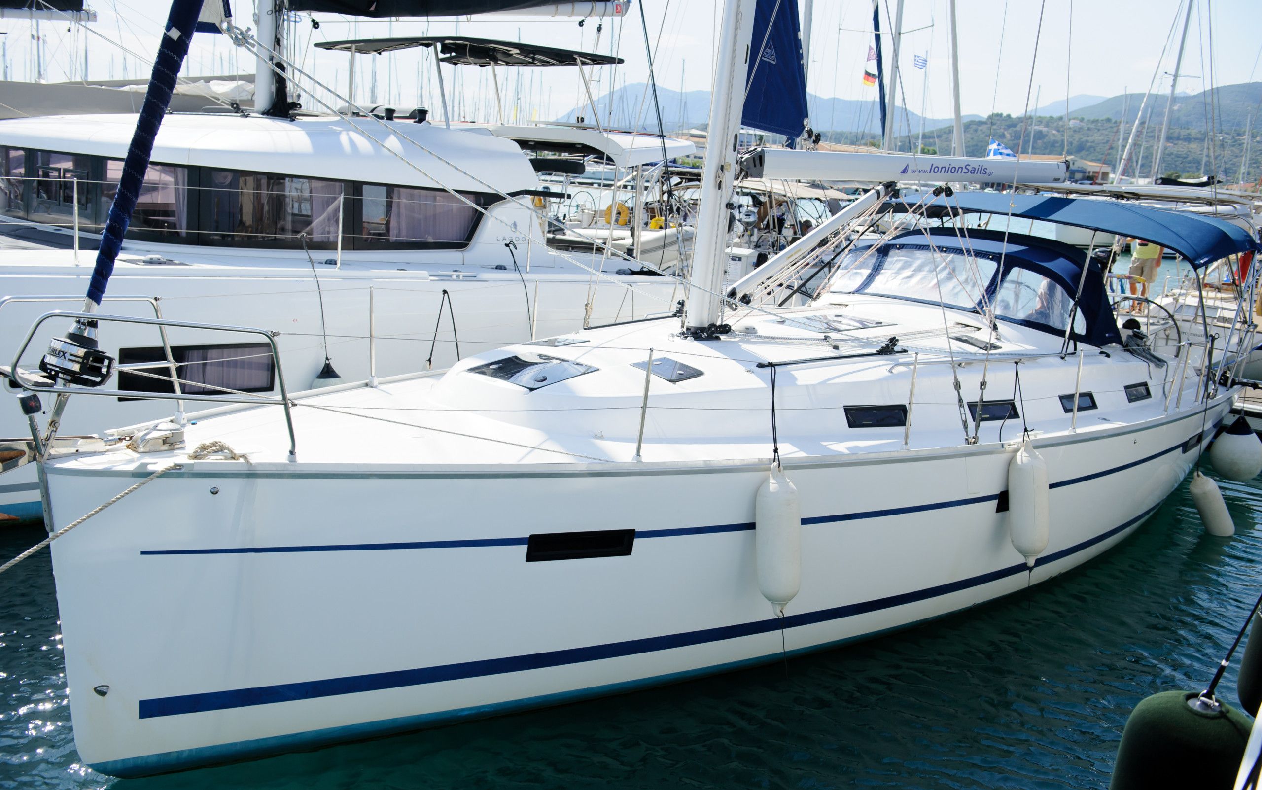 En vit yacht låg förtöjd vid en småbåtshamn och hade en blå rand längs skrovet, omgiven av andra båtar.