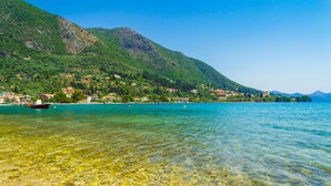 A clear lake with a boat, a mountain, and buildings along the shore. - Sun-soaked Sailing Adventure in the Ionian Islands (Perigiali)