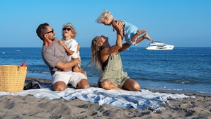 Een gezin op het strand met een picknickmand en een boot op de achtergrond.
