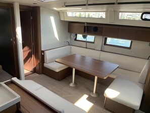 A compact boat interior with a dining area, cushioned seating, and windows providing views of the water. - Sun-Kissed Sailing Adventure in Islas Sarónicas (Rodos)