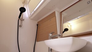 Un baño con un lavamanos blanco, un cabezal de ducha de mano y un espejo.