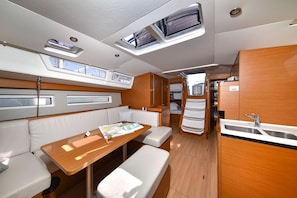 A compact kitchen with a sink, a dining area with a table and benches, and a small seating area with cushions. - Sun-Kissed Sailing Adventure in Zadar, Croatia (Bibinje)