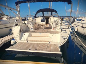 Ein Boot liegt in einer Marina festgemacht und hat ein Holzdeck, ein Steuerrad und den Namen 'Milky Way', der seitlich sichtbar ist.