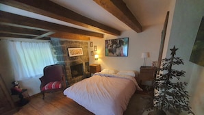 A bedroom with a bed, a chair, a fireplace, and a wall-mounted lamp.