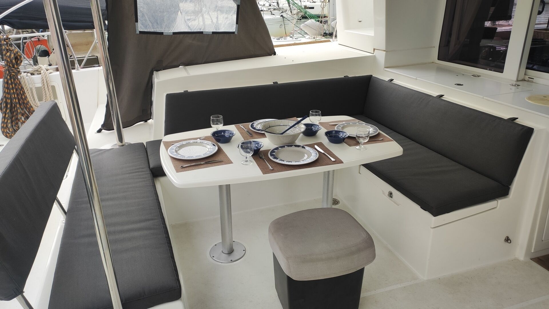 Interior de barco moderno y compacto, con zona de comedor que incluye una mesa preparada para cuatro personas, rodeada de asientos acolchados.