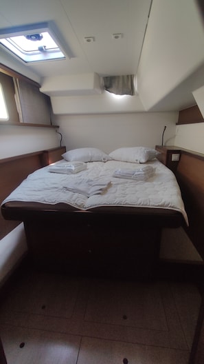 Ein kleines Zimmer mit einem Einzelbett, einem Dachfenster, einem schmales Fenster und einem Kopfteil mit Nachtisch.