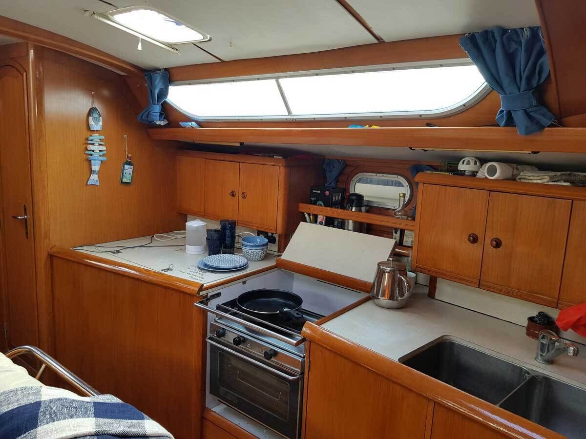 A compact galley with a stove, oven, sink, and wooden cabinetry.