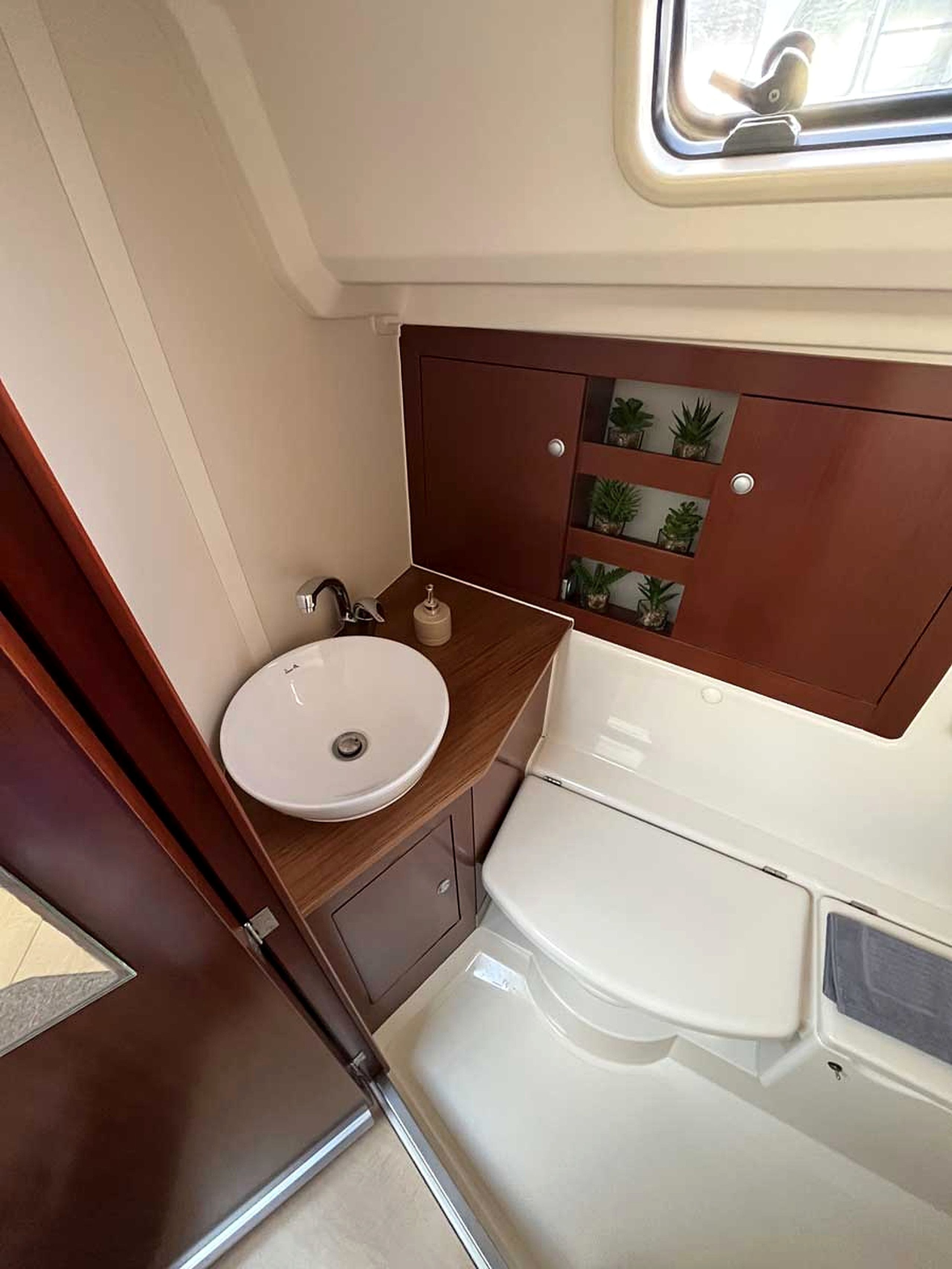 A compact RV bathroom with a sink, toilet, and a small window.