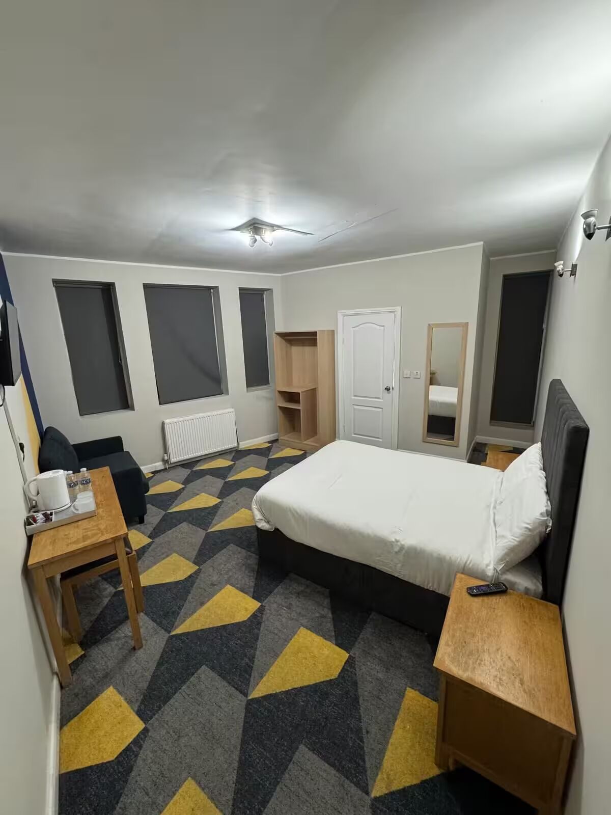 A hotel room with a bed, a desk, a chair, a wardrobe, and a mirror.