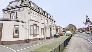 Un edificio histórico con un letrero que dice 'WEASTE HOTEL', una calle pavimentada y una señal de tráfico que indica 'Baches por 280 metros'.