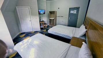 A hotel room with two beds, a desk, a TV, a wardrobe, and a door.