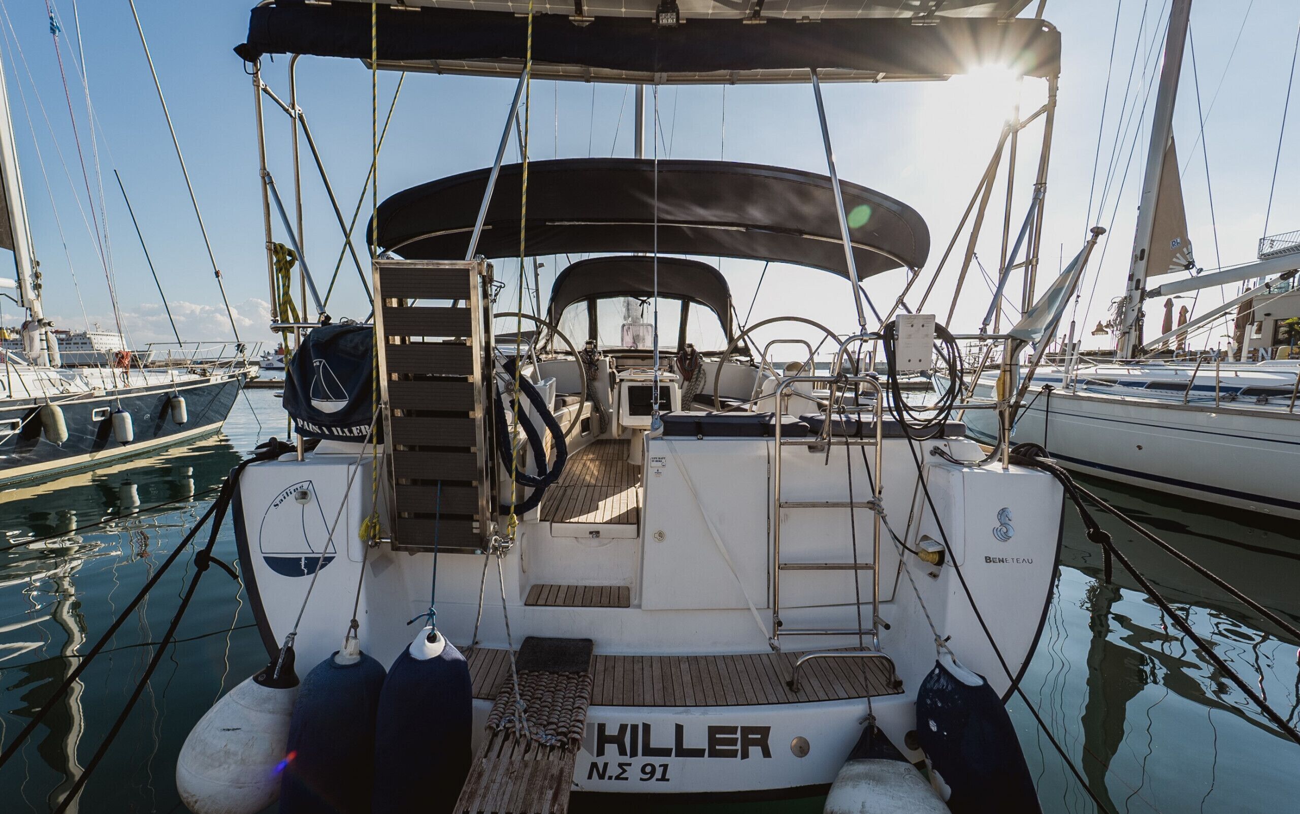 A sailboat named 'KILLER' docked at a marina with a covered deck, winches, and a lifebuoy.
