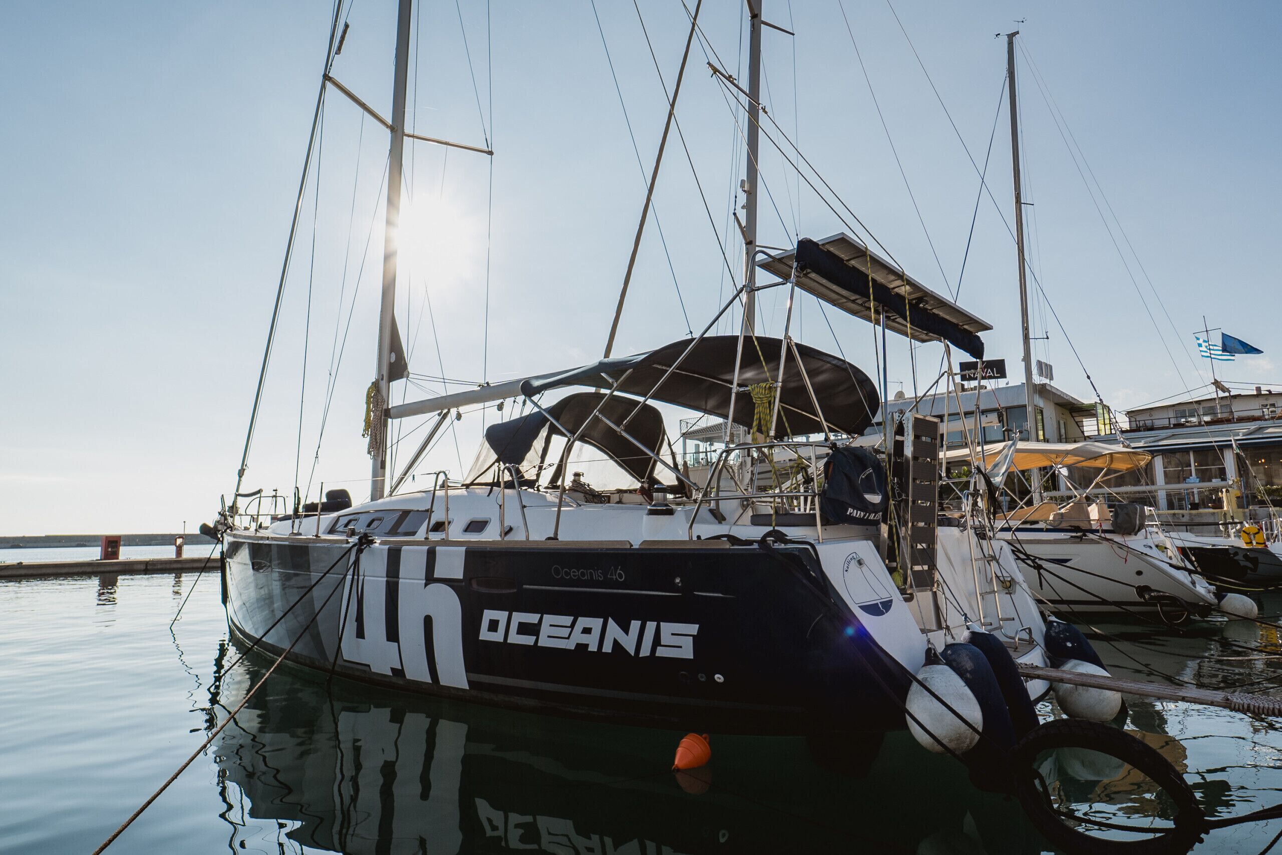 Un voilier baptisé « OCEANIS » était amarré dans une marina, aux côtés d’autres bateaux, sous un ciel dégagé et sur une eau calme.