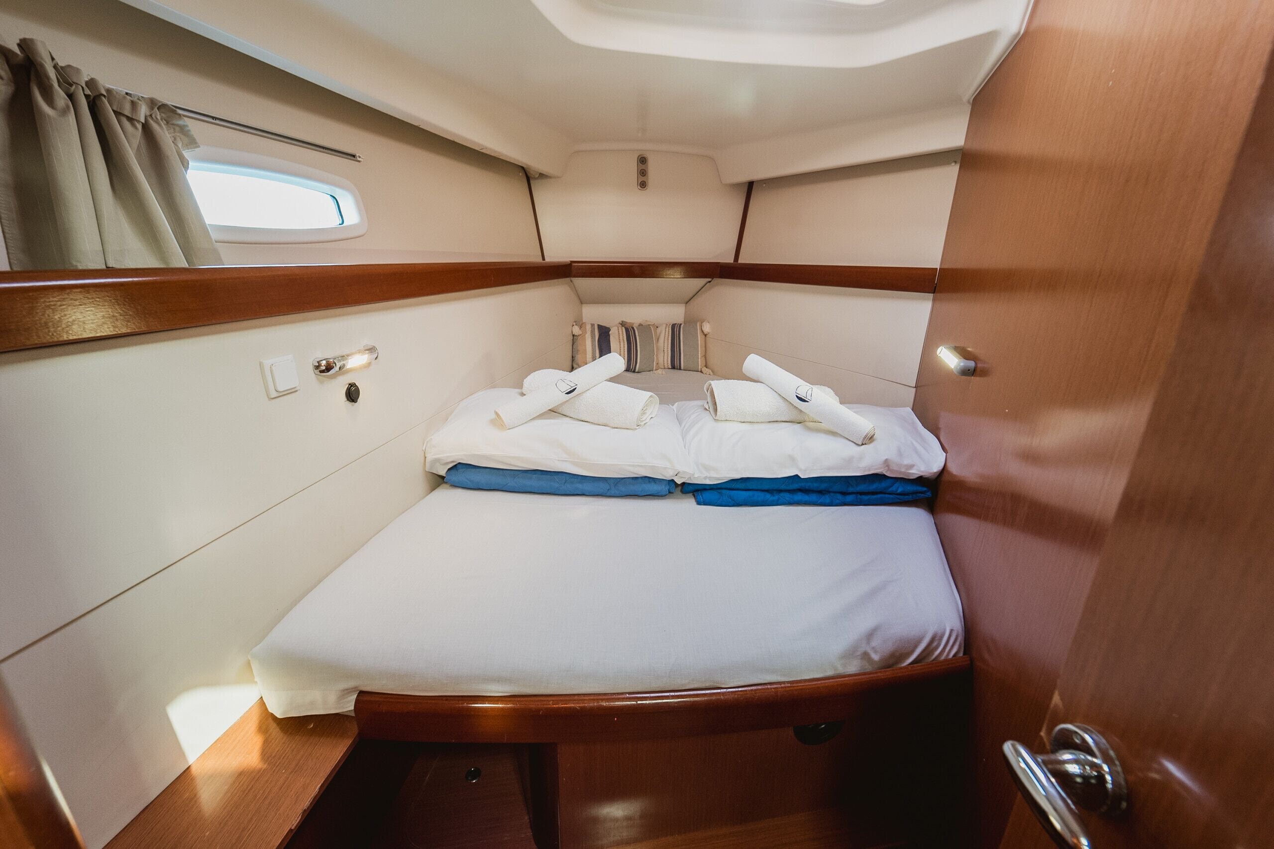 Une cabine compacte comprenant un lit simple, une fenêtre avec des rideaux et un petit luminaire au plafond.