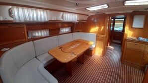 Interior de un barco con una mesa de madera, asientos acolchados y una pequeña cocina.